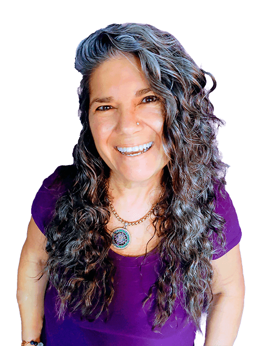 Smiling woman with long curly grey hair, wearing a purple top and a gold necklace.