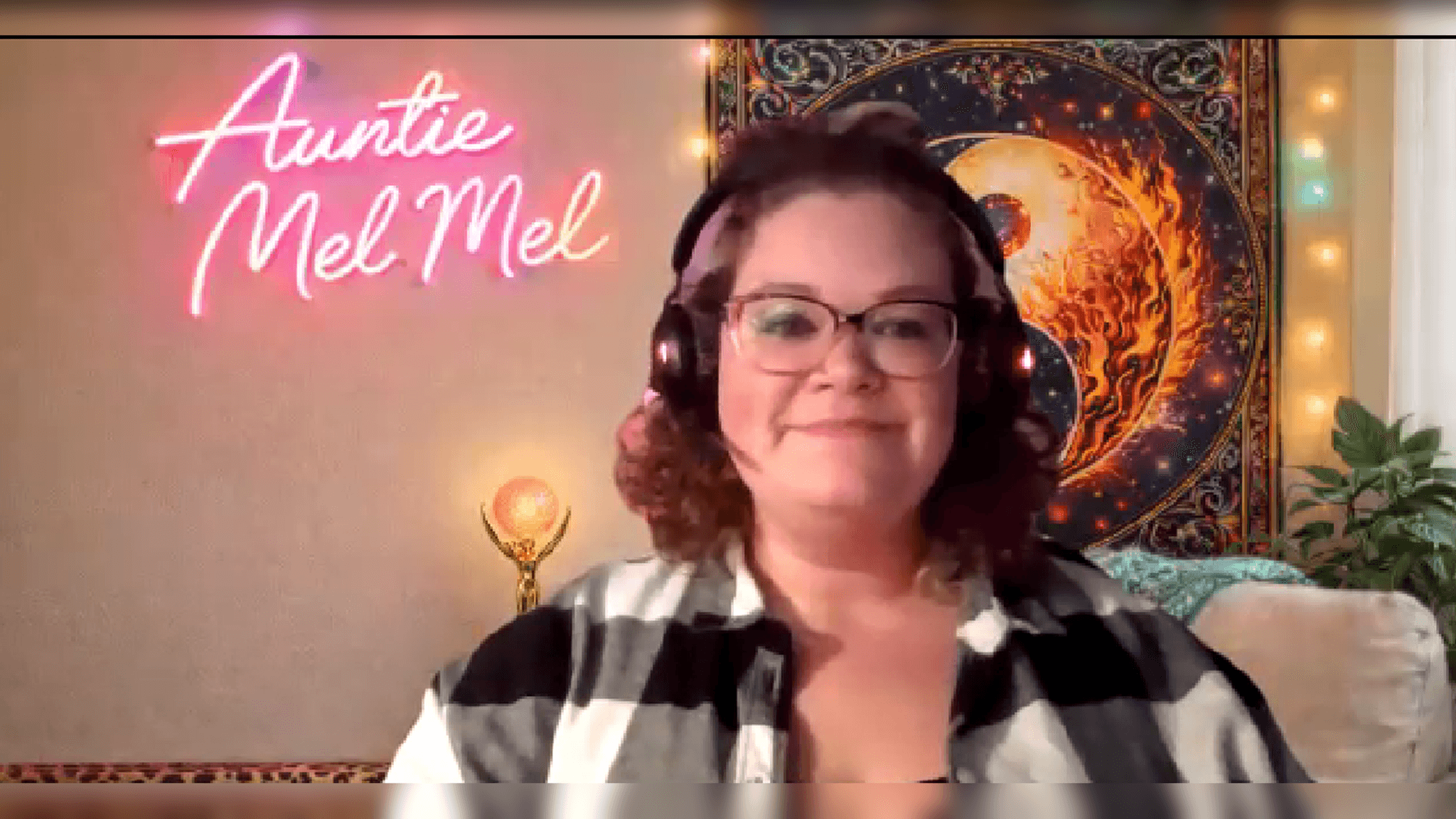 Smiling woman with glasses and headphones before a pink neon sign and decorative tapestry.